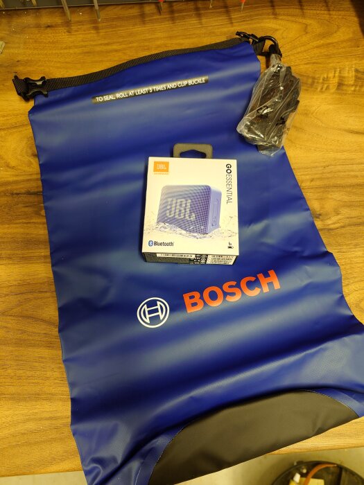 En blå vattentät Bosch-väska på ett bord, med en förpackad JBL Go Essential Bluetooth-högtalare ovanpå.