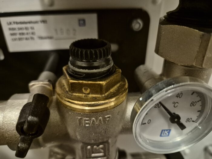 Termostatens rör med mässingsfärgad del märkt "TEMP", bredvid en termometer som visar cirka 22°C.