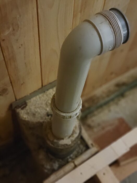 Avloppsrör under diskbänk i köket, går ner i gjuten betongplatta, plastmaterial som kan vara en del av renoveringsfråga om byte av rör.