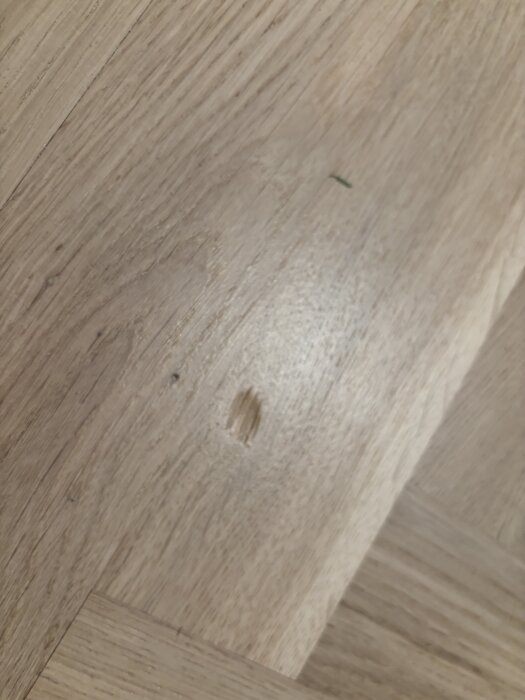 Märke på nylagd parkett med träkornsmönster, visar ett djupt jack i golvet.