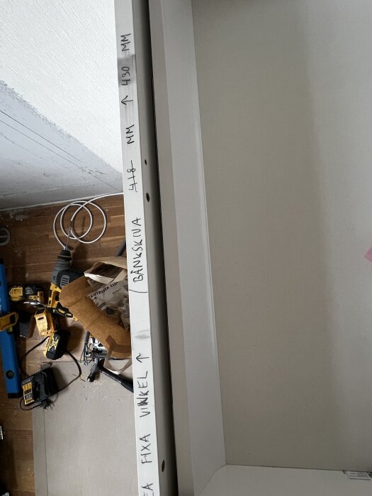 Text på en bänkskiva med instruktionerna "IKEA fixa vinkel" och mätningar, omgiven av verktyg och kablar på byggarbetsplats.