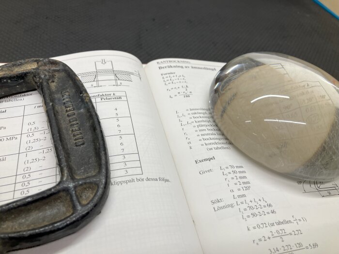 En reading stone ligger på en uppslagen bok med teknisk text och diagram. Bredvid finns ett metallobjekt med text.