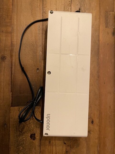 Vit elektroniklåda med sladd på träbord, märkt "Uponor".