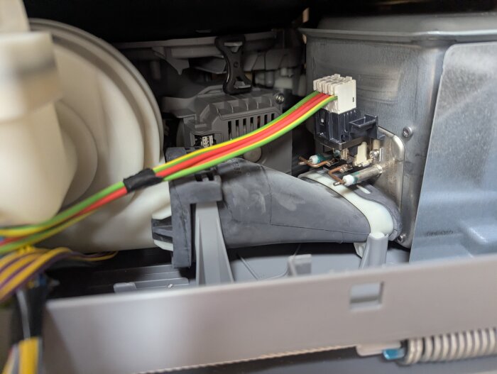 Inre delen av en torktumlare med synliga kablar och anslutningar, där luftkanalen och en komponent av plast är i fokus.