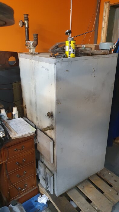 Äldre Diom pannan, el och olje kombi, står på träpall bredvid träbyrå med papper och verktyg ovanpå.