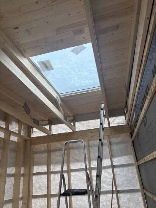 Takfönster monterat i trästomme, med stege under. Solceller och isolering synliga efter stomresning.
