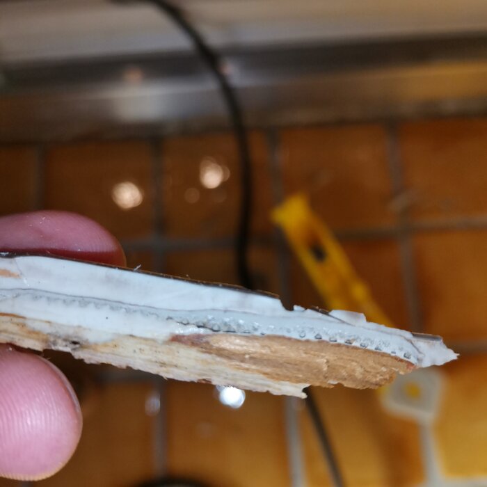 Närbild av träliknande material lager med silikonfog, borttaget från badrumsgolvet vid dusch.