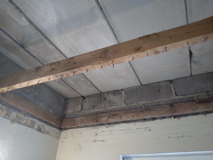 Tak med betongskivor och träram i ytterhall under renovering, sprickor synliga i byggstrukturen.