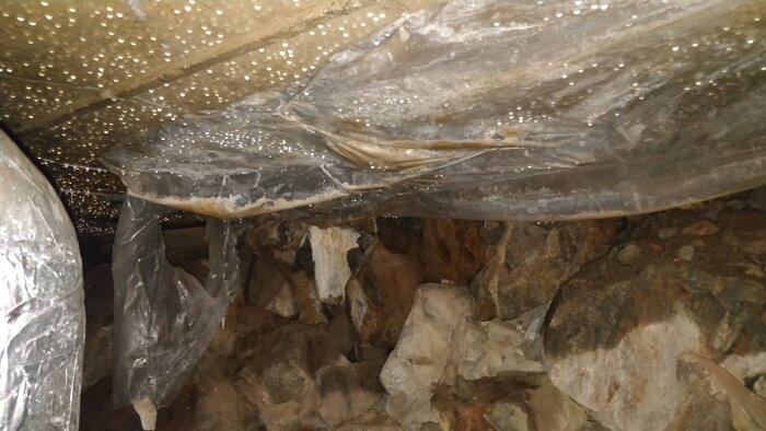 Plastic sheeting is partially embedded in concrete, collecting condensation and debris, visible against a rocky surface.