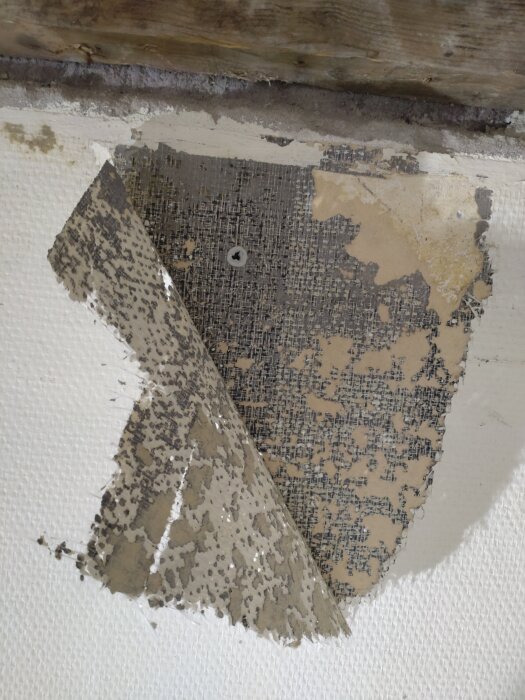 En vägg med avdragen målad glasfiberväv som avslöjar tapet under i ett renoveringsprojekt.