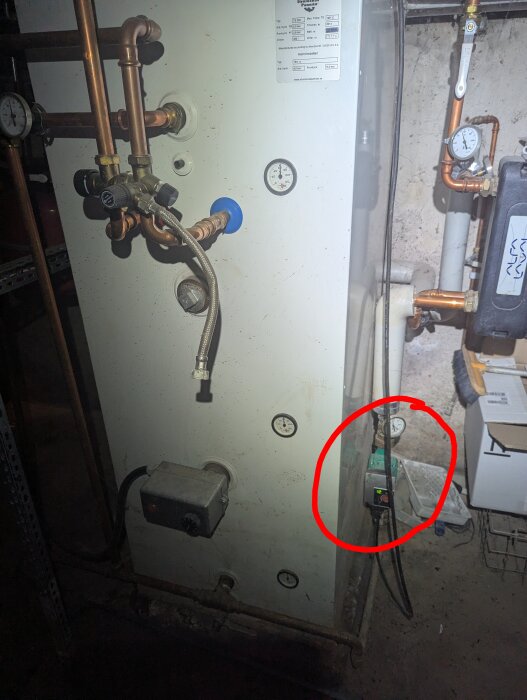 Cirkulationspumpar i ett badrums radiatorsystem, inringade, med kopparrör i förgrunden och en tryckmätare till höger.