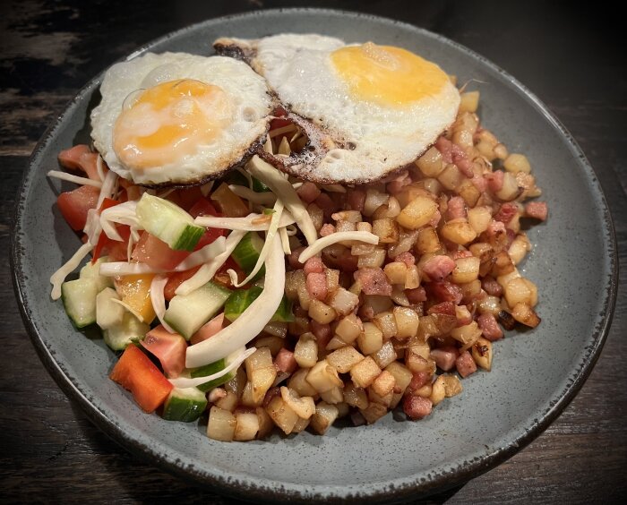 En tallrik med krögarpytt, stekta ägg och sallad med gurka och tomat.