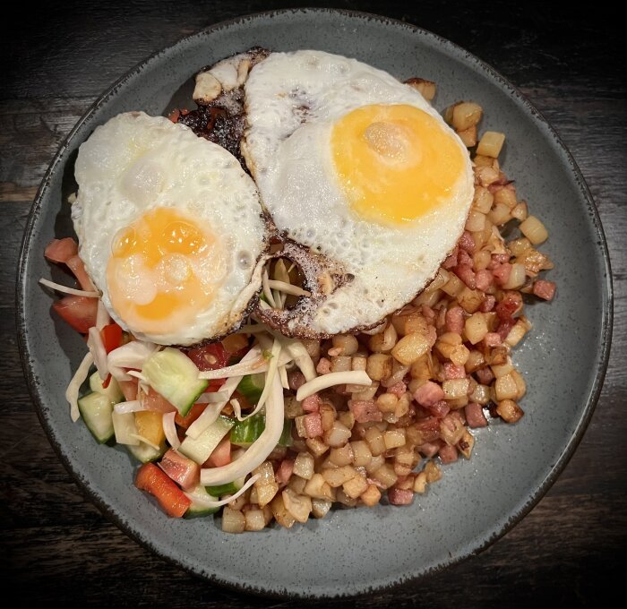 Tallrik med krögarpytt, sallad och två stekta ägg med solig sida upp.