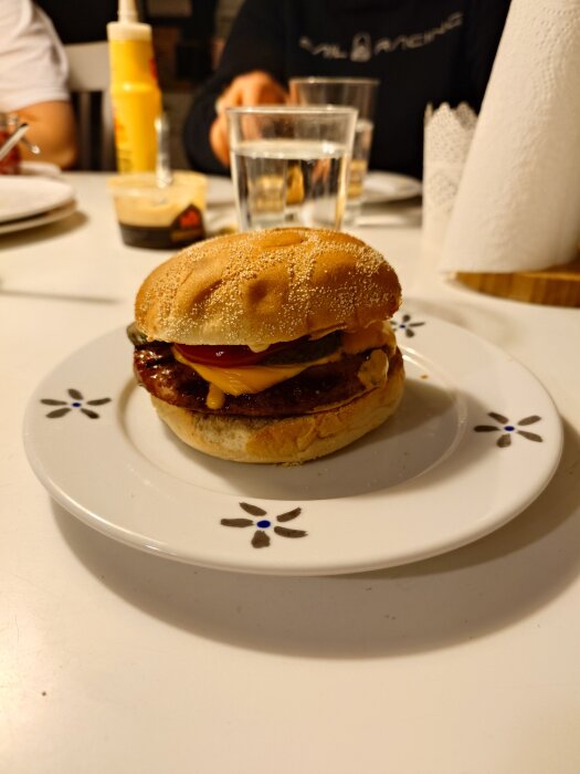 Hamburgare på fat med Frisco-bröd, ost, rostad och picklad lök, saltgurka, gul senap, ketchup, sourcreme-peppar på bord med senapstub och papper.