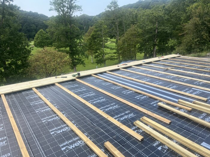 Reglar läggs på webertec-membran i skogslandskap; verktyg synliga på byggplatsen.