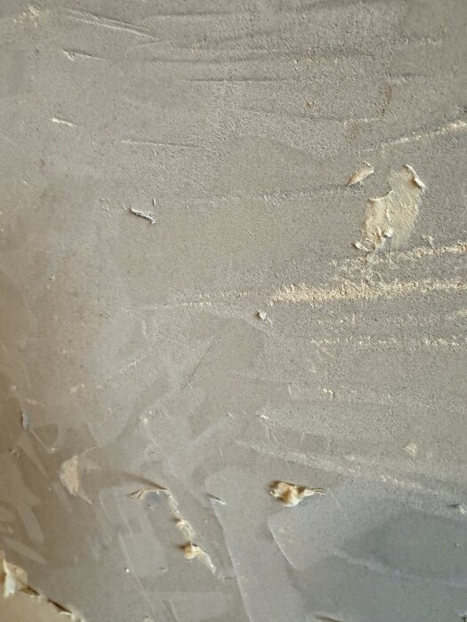 Grå massa mellan tapetlager, med ojämn yta och sprickor. Personen undrar om det kan innehålla asbest vid renovering.