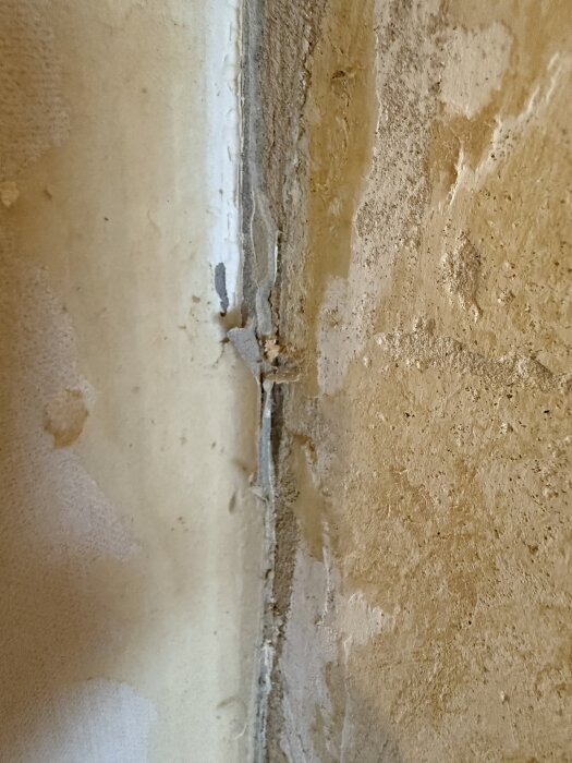 Vägg med lager av tapeter, mellanlagret visar en grå massa, osäker på om det innehåller asbest.