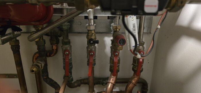 Rörledningar och avstängningsventiler i en fjärrvärmecentral, inklusive röda och svarta ventiler samt kopparrör.