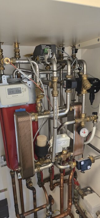 Fjärrvärmecentral med rördragning, ventiler och termostat med Honeywell-panel, inkluderar Grundfos pump, i installationsutrymme.