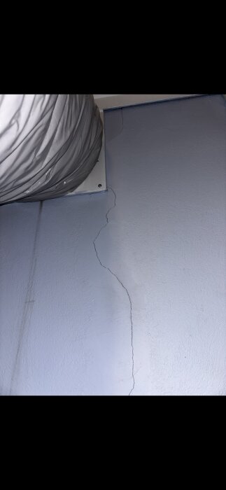 Spricka i en vägg i ett 70-tals hus, med en stor luftkanal ovanför, fotograferad inomhus.