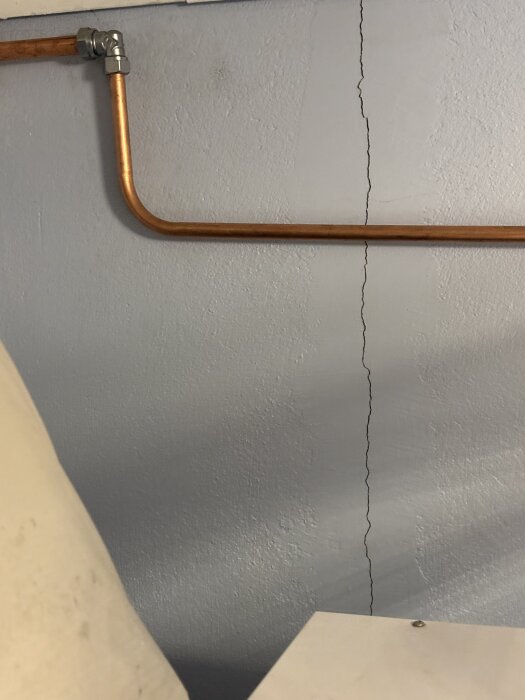 Vägg med en vertikal spricka bredvid en kopparledning, indikerande möjliga problem i ett 70-tals hus.