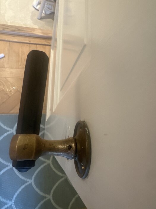 Gammaldags dörrhandtag i mässing sitter fast på trädörr, närbild visar avbrutet skruvhuvud.