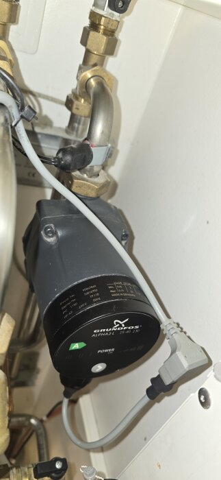 Cirkulationspump från Grundfos, modell ALPHA2L, monterad i ett rörsystem. Synligt elanslutning och rörkopplingar med mässingsbeslag.