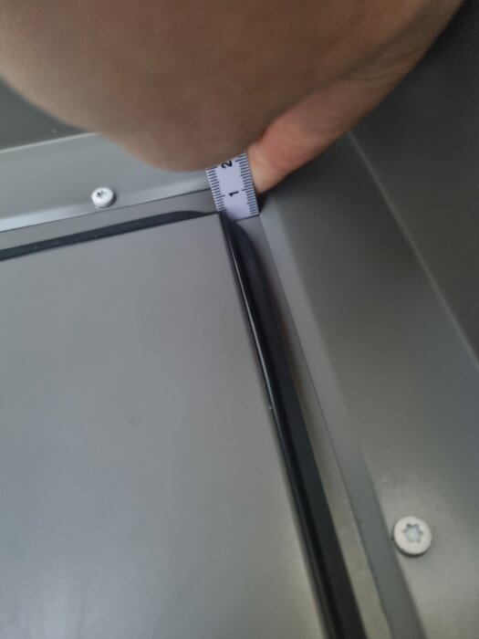 Närbild av dörrens högra sida där en måttband används för att mäta avståndet mellan dörrbladet och karmen.