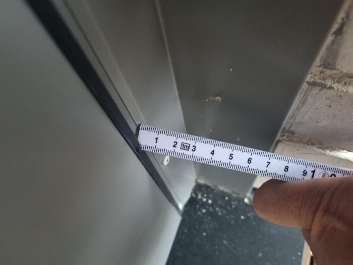 Närbild av en dörrkant med måttband som visar ett glapp på ungefär 5 till 6 mm mellan dörrbladet och karmen.