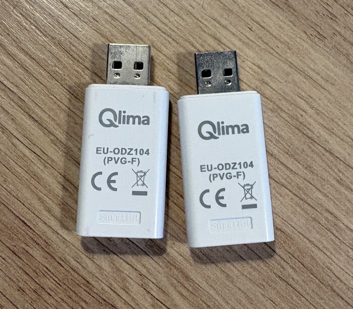 Två Wi-Fi-stickor för Qlima AC/LLVP med modellnummer EU-ODZ104 (PVG-F) liggandes på ett träbord.