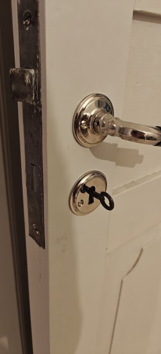 Dörr med blankt metallhandtag och lås med nyckel isatt, installerat för att ersätta en eventuell hasp.