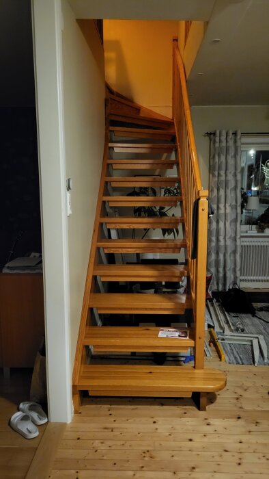 Lackad furutrappa, med vangstycken och räcke, i ett hem med neutrala väggar och dekor i bakgrunden.