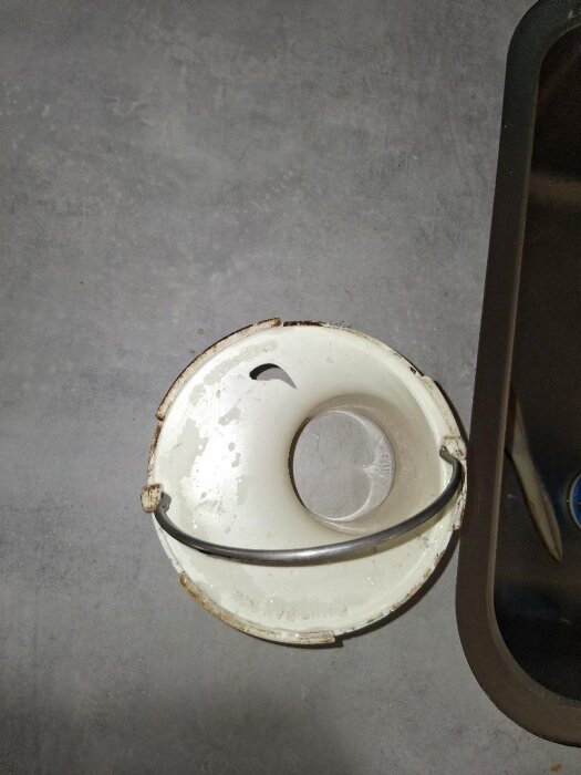 Golvbrunnsinsats med märke Ran RSK 711 80 82, vit med ett runt metallhandtag över, synligt hål vid sidan.