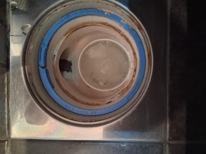 Golvbrunn med en blå och rostig insats, märkt Ran RSK 711 80 82 AB Sjöbo Bruk, visar skador och problem att hitta ersättningsdel.