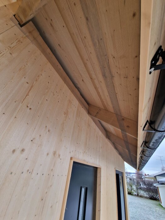 Byggnad med träfasad, visande underspikning med insektsnät och takränna.