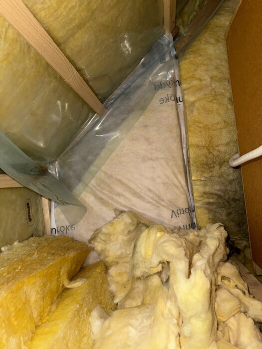 Mineralullisolering i en oorganiserad hög på en kattvind, träbjälkar och plast synliga, del av en diskussion om stark kemisk lukt.