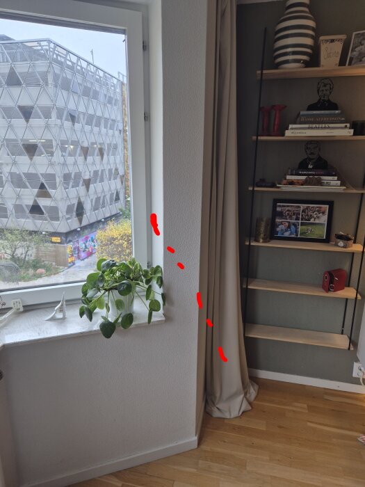 Vägg med burspråk och rödmarkerad väg för vp-rör, bredvid en hylla och ett fönster med växt. Bakom fönstret syns en byggnad.