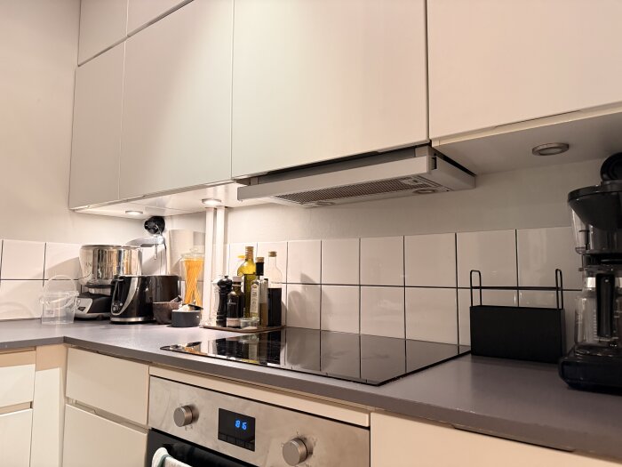 Takmonterade spotlights ovanför en köksbänk, där spotlighten längst till höger har slutat fungera. Köksapparater, spis och flaskor syns på bänken.