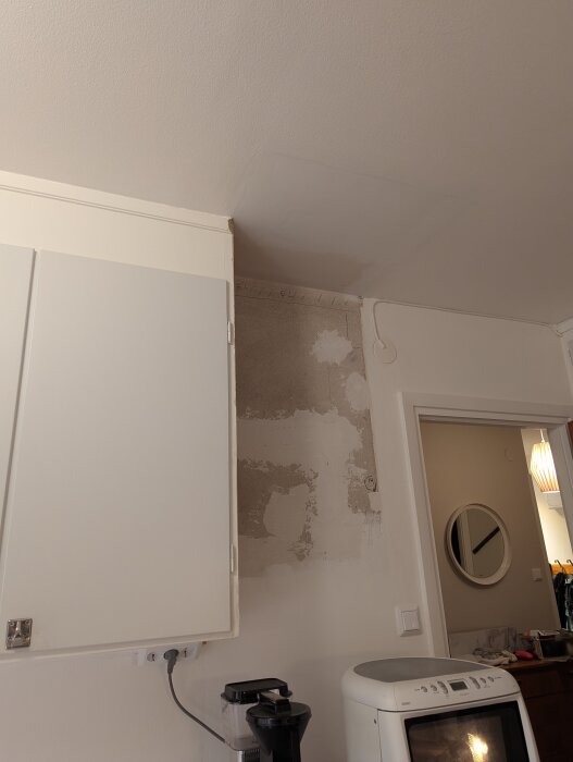 Tak med fläckar ovanför köksskåp, synliga skillnader i målarstruktur och glans. Väggfläckar finns framför köksmaskin och intill dörröppning.