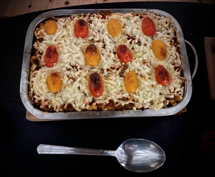 Pastagratäng med ost, tomater och köttfärs i en ugnsform, serverad med en sked.