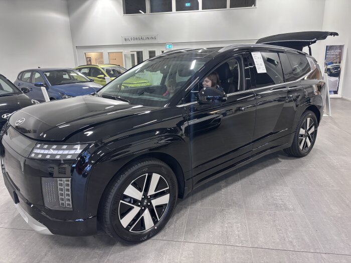 Svart Hyundai Ioniq 9 står i ett bilshowroom, med en person i förarsätet och bakluckan öppen.