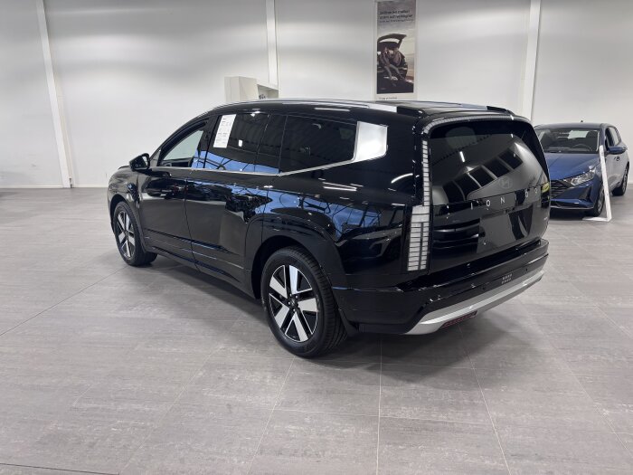 Svart Hyundai Ioniq 9 i en bilhall, sedd bakifrån med reflektioner på karossen och ett annat fordon i bakgrunden.