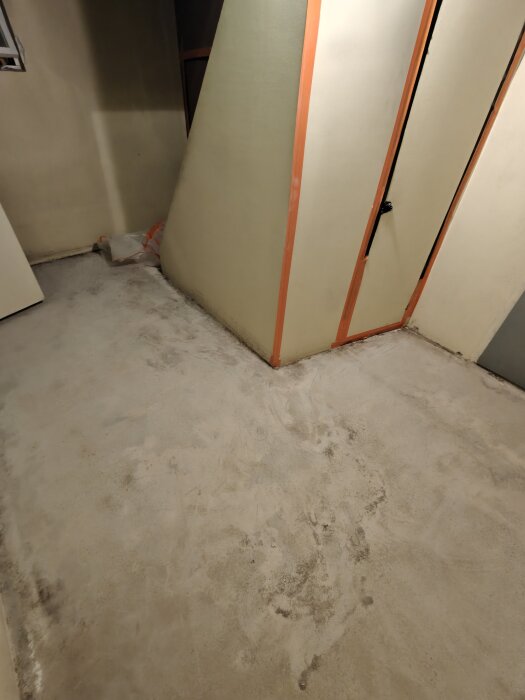 Slipat betonggolv i ett 50-talshus källare, med en orange och beige vägg och en plastpåse i hörnet.