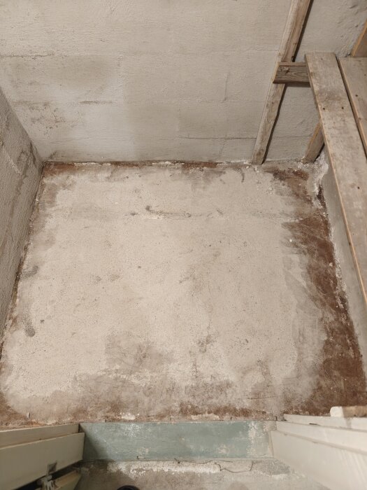Slipad yta av betonggolv i ett källarrum, med bruna fläckar och synlig murad vägg i ett äldre 50-talshus.