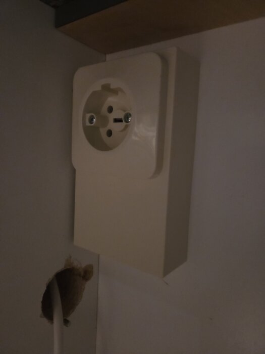 Perilex-uttag monterat på en vägg, med synlig kabel genom ett borrat hål nedanför.