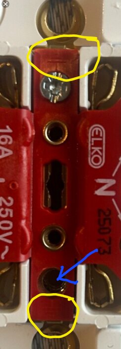 Närbild av jordsymboler markerade i gult på ett uttag. En skruv saknas vid den jordanslutning som den blå pilen pekar på.