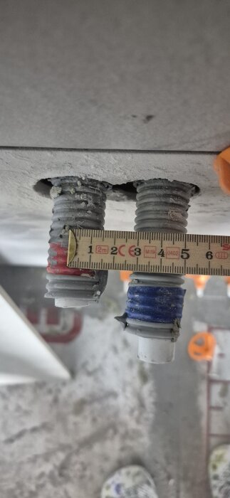 Två vattenrör i betonggolv, avstånd mätt med linjal visar 40 mm cc. Ena röret har blå märkning, båda med metallringar.