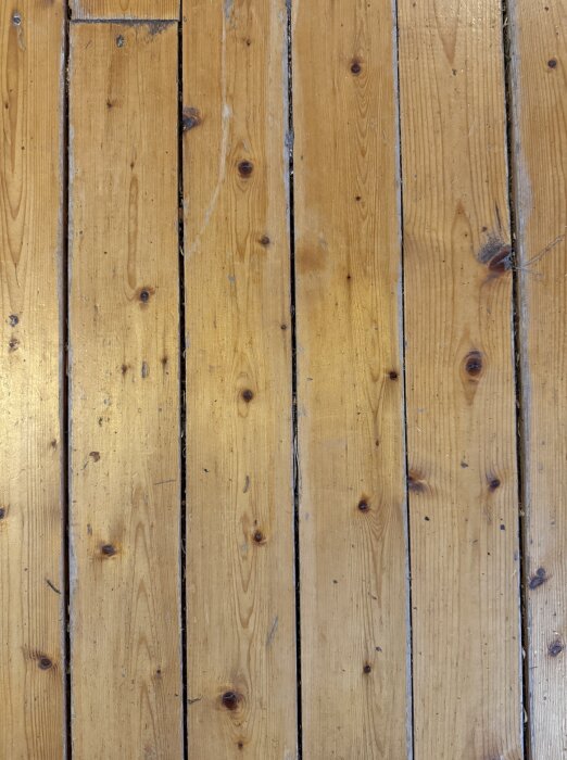 Furugolv från 70-talet med synliga springor mellan plankorna, träets yta är något sliten men har en varm ton och tydliga årsringar.