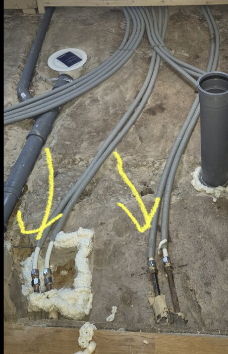 Skarvar av rör på betonggolv med skumisolering, markerade med gula pilar.