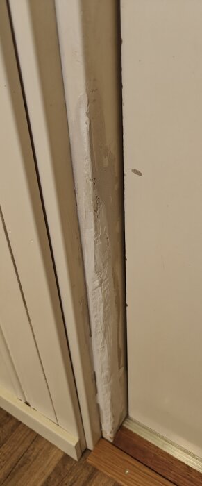 Skadad dörrkarm med spackelförsök på träet, eventuella klösmärken, belägen vid en ljusmålad ytterdörr och trägolv.